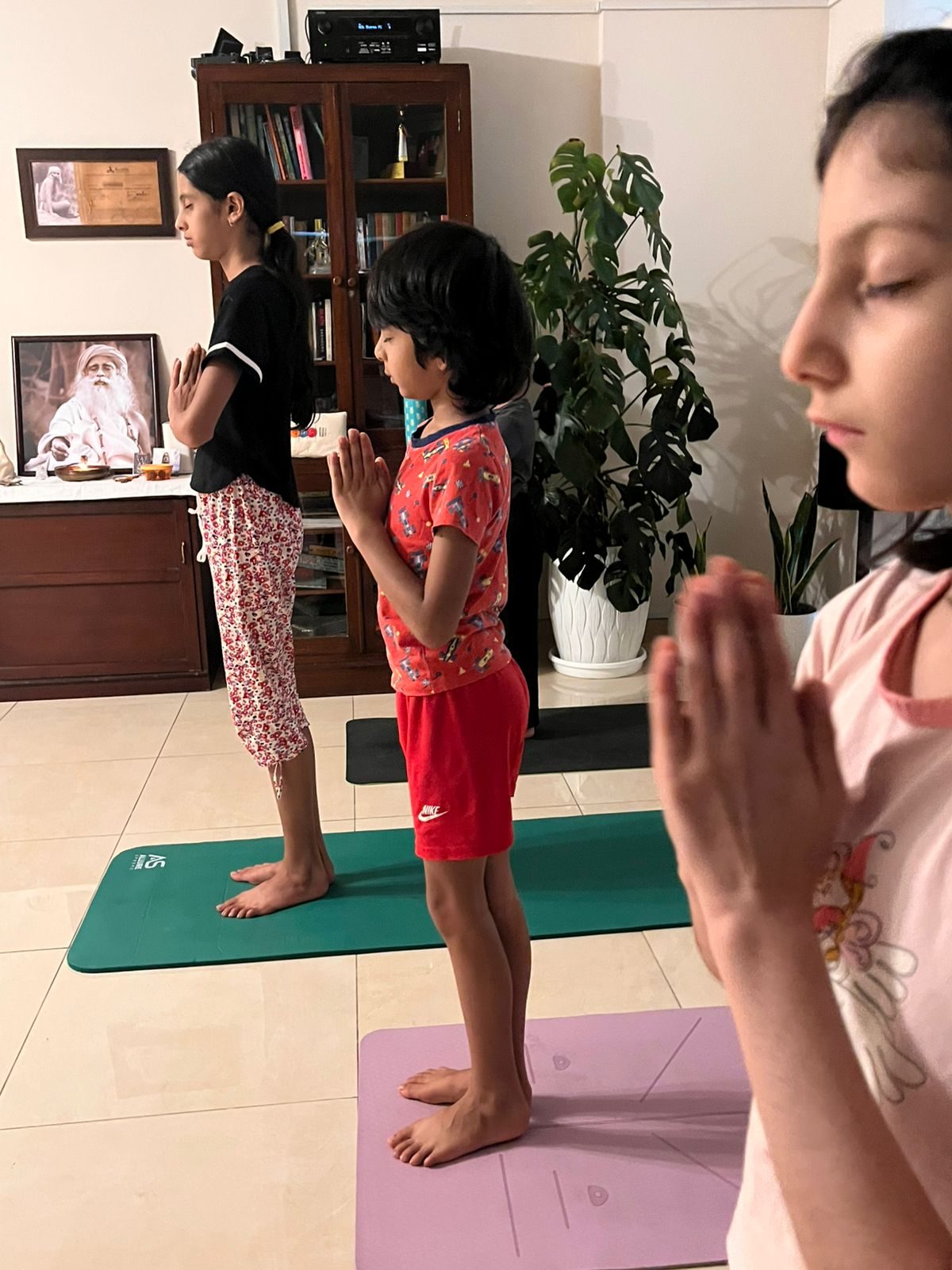 Three children standing on their mats, palms together at the chest, eyes closed